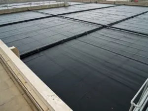 Black HDPE geomembrane floating cover on a wastewater lagoon with ballast troughs